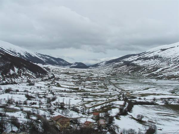 Snowy village in mountain valley, red-roofed houses, cloudy sky