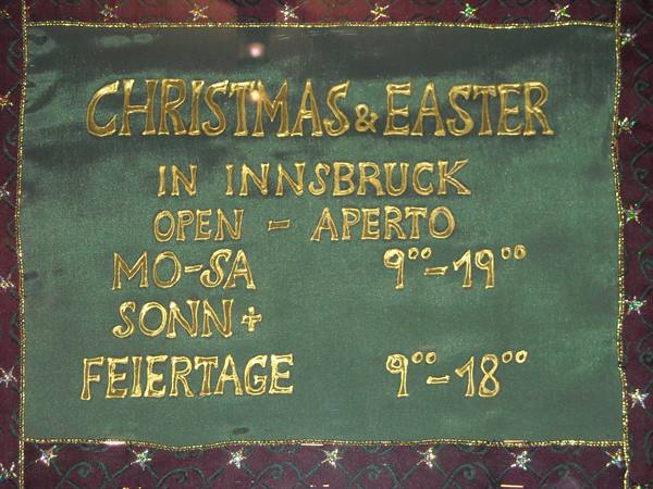 Green fabric sign with gold embroidery showing Innsbruck opening hours