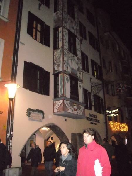 Tourists at night beneath a frescoed building, Gasthof Weisses Kreuz sign
