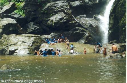 Tourists swim in the pool beneath a waterfall among rocks