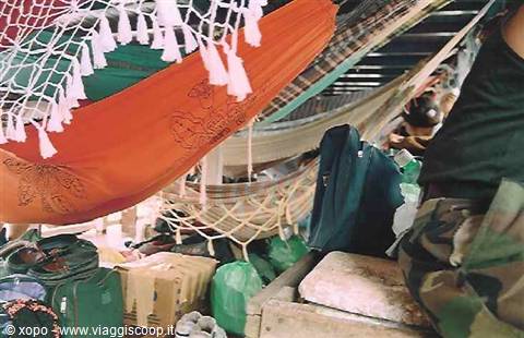 Tangled colorful hammocks and backpacks piled in a crowded hold, natural light