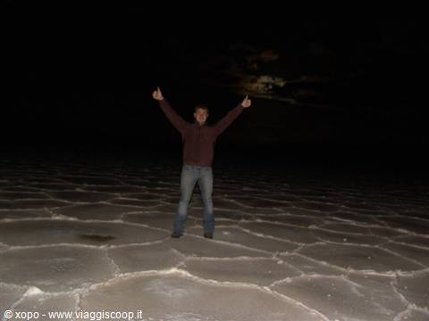 Tourist with raised arms at night on Salar de Uyuni, lit salt crusts