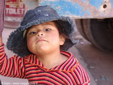 Child in blue hat and red striped sweater beside an old truck
