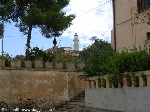 Old stone wall with steps, trees and a white lighthouse among houses