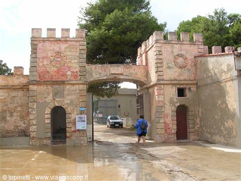Man walks under the arch of an old fortified stone gateway with crenellated towers