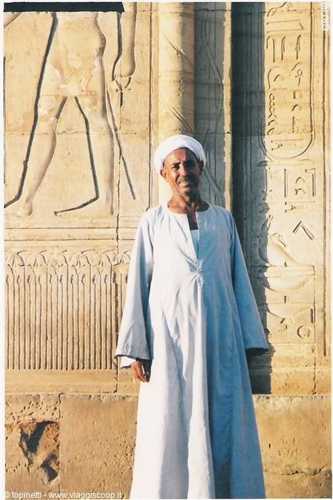Man in white galabeya and turban before carved hieroglyphs of the temple