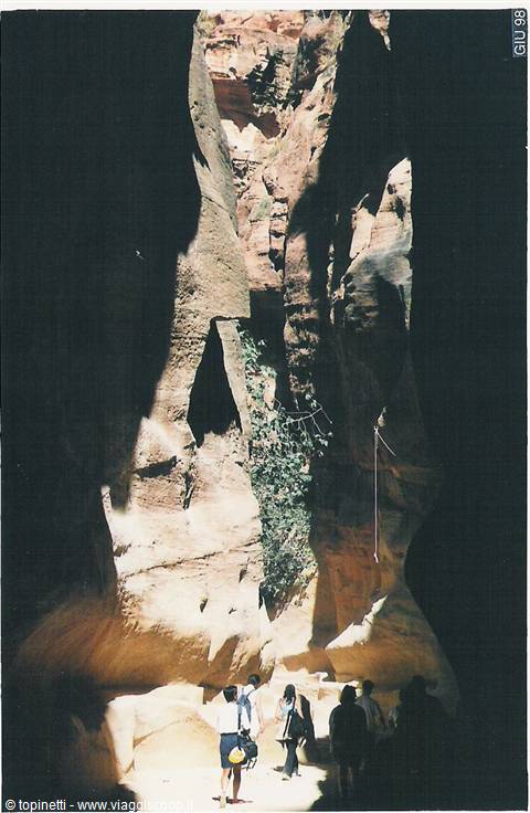 Tourists walk through the Siq of Petra between towering rose rock walls
