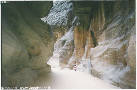 Tourist walks through the Siq of Petra, sandstone canyon walls glowing in sunlight