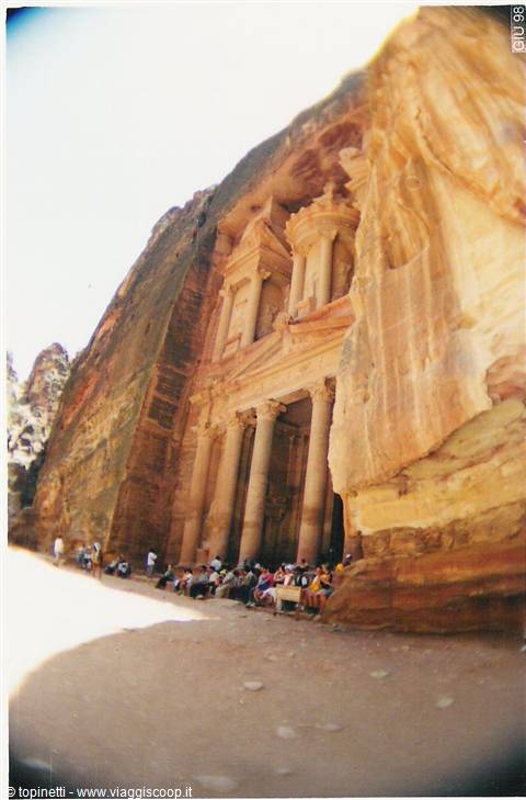 Tourists sitting in front of Petra's Treasury, facade carved in pink rock