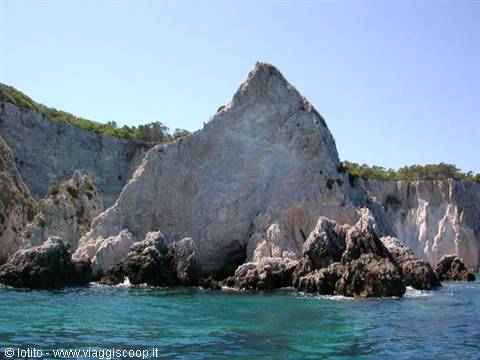 Large white limestone rock formation before cliffs, turquoise sea, clear sky