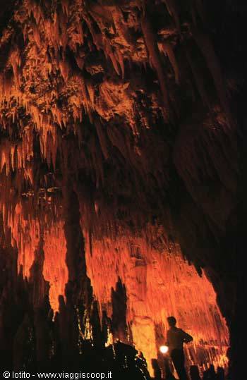 Visitor with torch among stalactites and rock columns lit in red