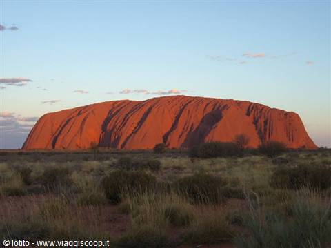 Uluru, huge red monolith rising above Australian scrubland under a clear sky