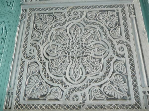White carved plaster panel with geometric floral patterns beside a green wall