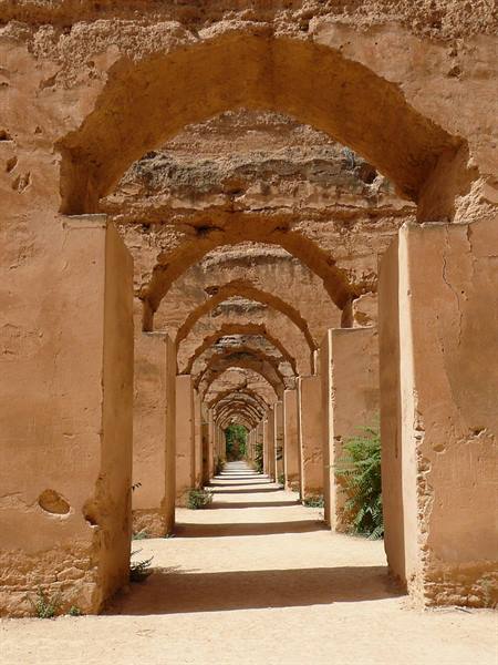Red-earth arches of Meknès royal stables, golden light between the pillars