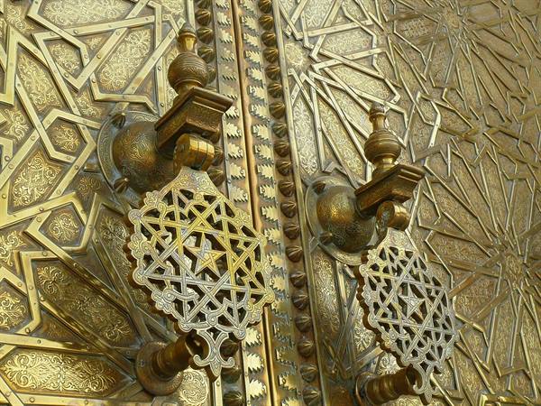 Ornate brass door knockers on geometric carved golden door