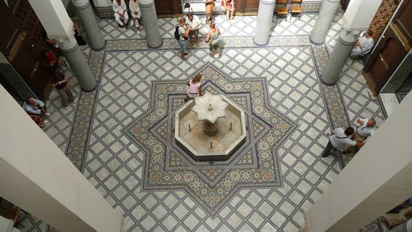 Tourists around an octagonal marble fountain, decorative tile floor, carved columns