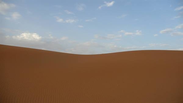 Red sand dune under blue sky with scattered clouds