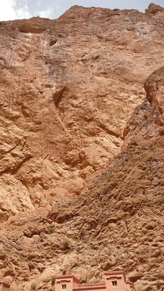 Reddish rock cliff towering over small brick houses, Todgha Gorge