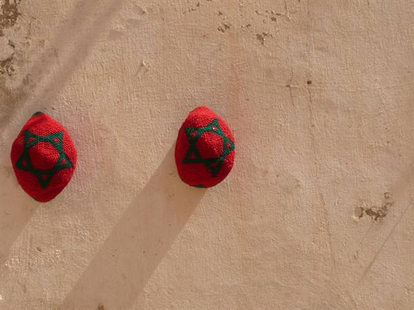 Two red fezzes with green star hanging on a plastered wall, diagonal shadow