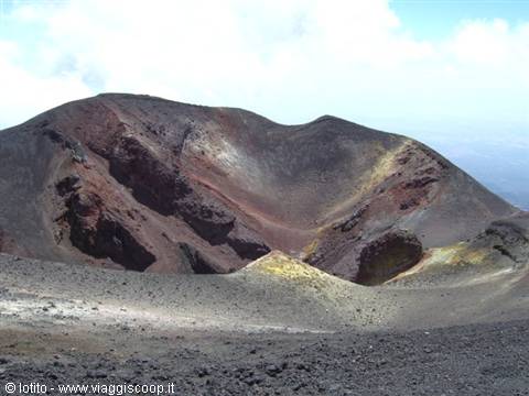 Volcanic crater on Mount Etna with red rocks and dark sand under white clouds