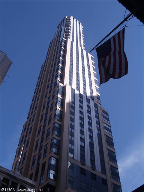 Sunlit stone skyscraper from below, American flag in the foreground