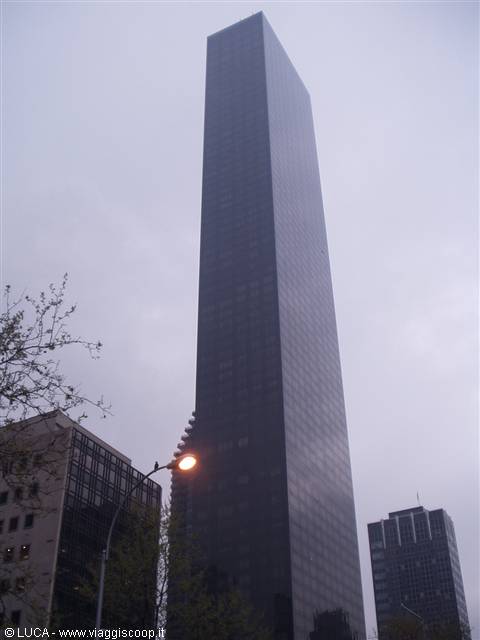 Dark glass skyscraper among buildings, lit streetlamp, overcast sky