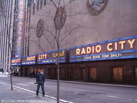 Man posing in front of the facade and neon signs of Radio City Music Hall