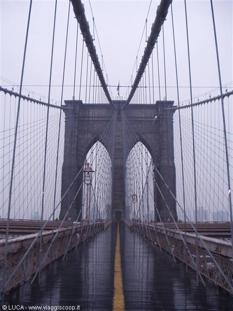 Brooklyn Bridge in the rain: wet wooden walkway, steel cables and stone tower