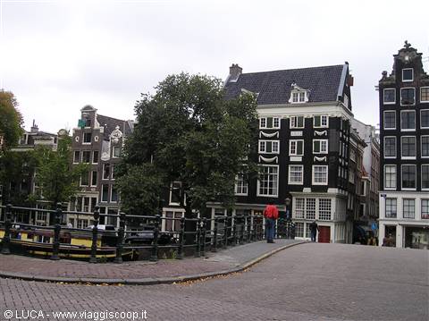 Tourist crossing a brick bridge among Amsterdam canal houses under grey sky