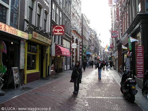 Pedestrians walking along brick Amsterdam street lined with coffee shops