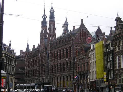 Magna Plaza in Amsterdam, red brick facade under grey sky, tram in street