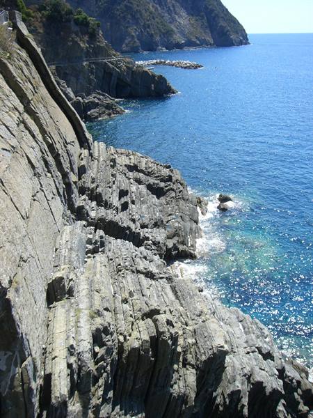 Layered rock cliffs above blue sea, coastal trail with hikers, Cinque Terre