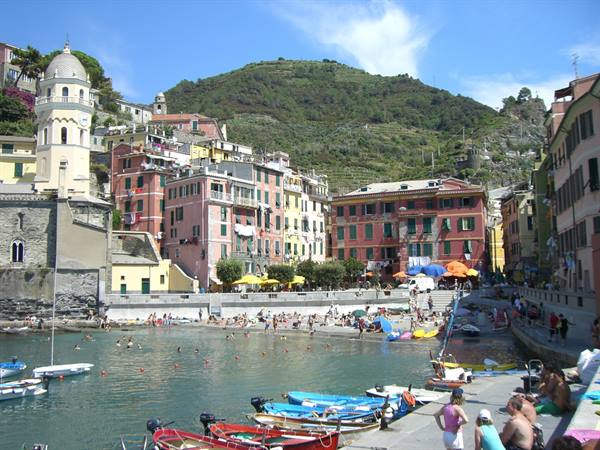 Vernazza: colorful houses, bell tower, moored boats and swimmers by the sea