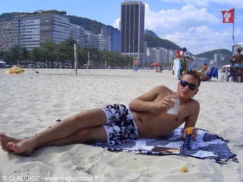 Guy lying on towel with drink, Copacabana beach, skyscrapers and mountains behind