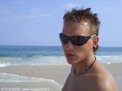 Young man with sunglasses and necklace on the beach by the sea