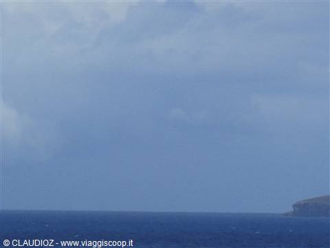 Cloudy sky over blue sea, dark rocky headland on the right horizon