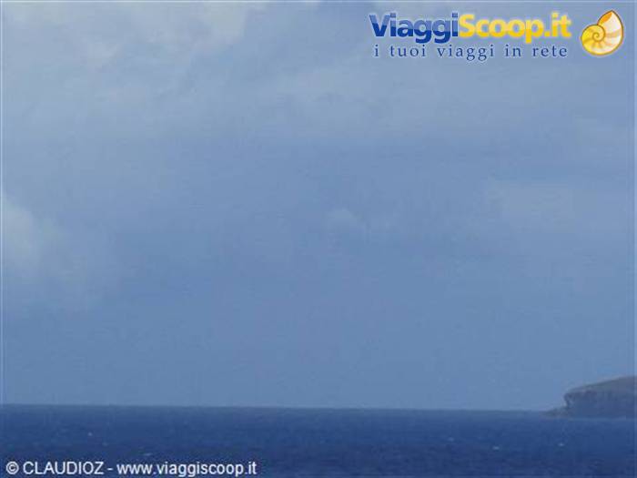 Cloudy sky over blue sea, dark rocky headland on the right horizon
