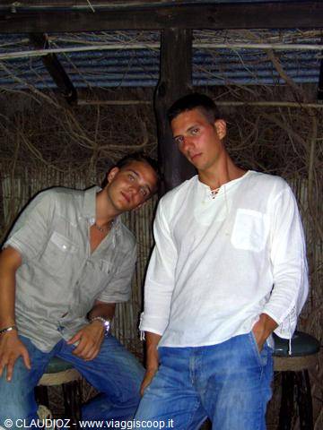 Two young men in jeans and white shirt sitting in a straw-walled bar