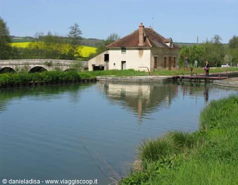 Stone house with tile roofs reflected in the canal, stone bridge behind