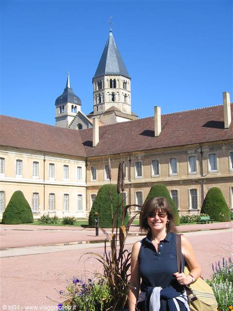 Smiling tourist in front of Cluny Abbey with stone towers and gardens