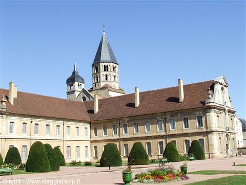 Cluny Abbey: courtyard with cone-shaped hedges, pale stone building and Romanesque towers
