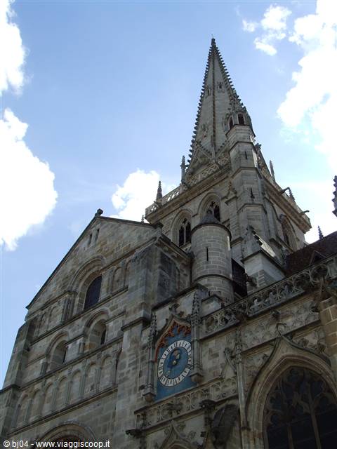 Gothic stone cathedral with spire and blue clock under cloudy sky