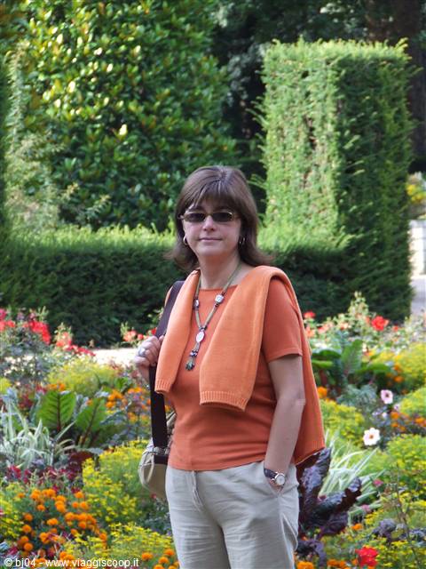 Smiling woman in orange top among clipped hedges and flower beds
