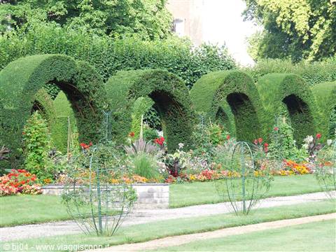 {"it": "Archway di bosso curvati sopra aiuole fiorite in un giardino"}, "en": "Curved boxwood arches over flowerbeds in a garden"}