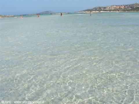 Crystal-clear shallow water over white sand, swimmers in the distance, Elafonisi
