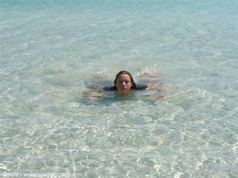 Woman lying in clear shallow turquoise water, sand visible below