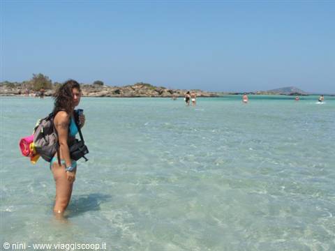 Girl with backpack wading in shallow turquoise water, rocks and swimmers nearby