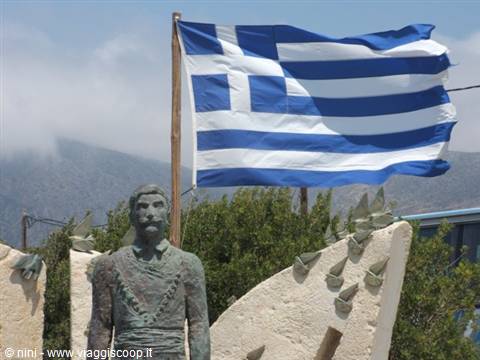 Stone statue of a man with a waving Greek flag in the background