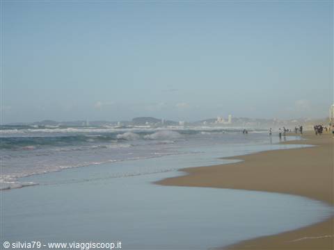 Small waves on wet sand, a few people walking along the seashore