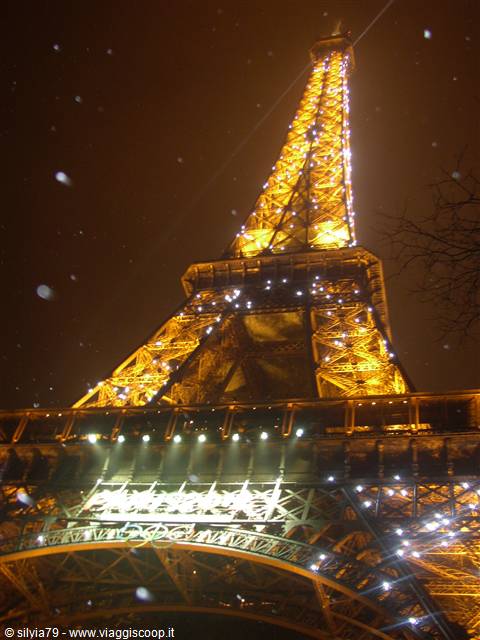Eiffel Tower lit up at night, golden ironwork with sparkling lights and falling snow